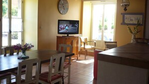 Un comedor con mesa de madera, sillas, televisor y un reloj en la pared.
