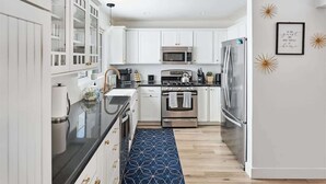 A modern kitchen with white cabinets, stainless steel appliances, and a blue patterned rug. - Eclectic & Stylish Home - Centrally located w/ heated pool, & more! (Phoenix)