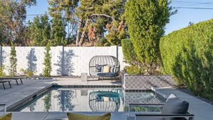 A swimming pool with a seating area, a white wall with a geometric pattern, and a hedge. - Eclectic & Stylish Home - Centrally located w/ heated pool, & more! (Phoenix)
