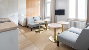 Une chambre d’hôtel moderne, équipée d’un canapé, de deux petites tables rondes, d’une télévision et d’une fenêtre avec des rideaux.