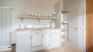 Une cuisine compacte avec des meubles blancs, un plan de travail en bois et une étagère intégrée au-dessus de l’évier.