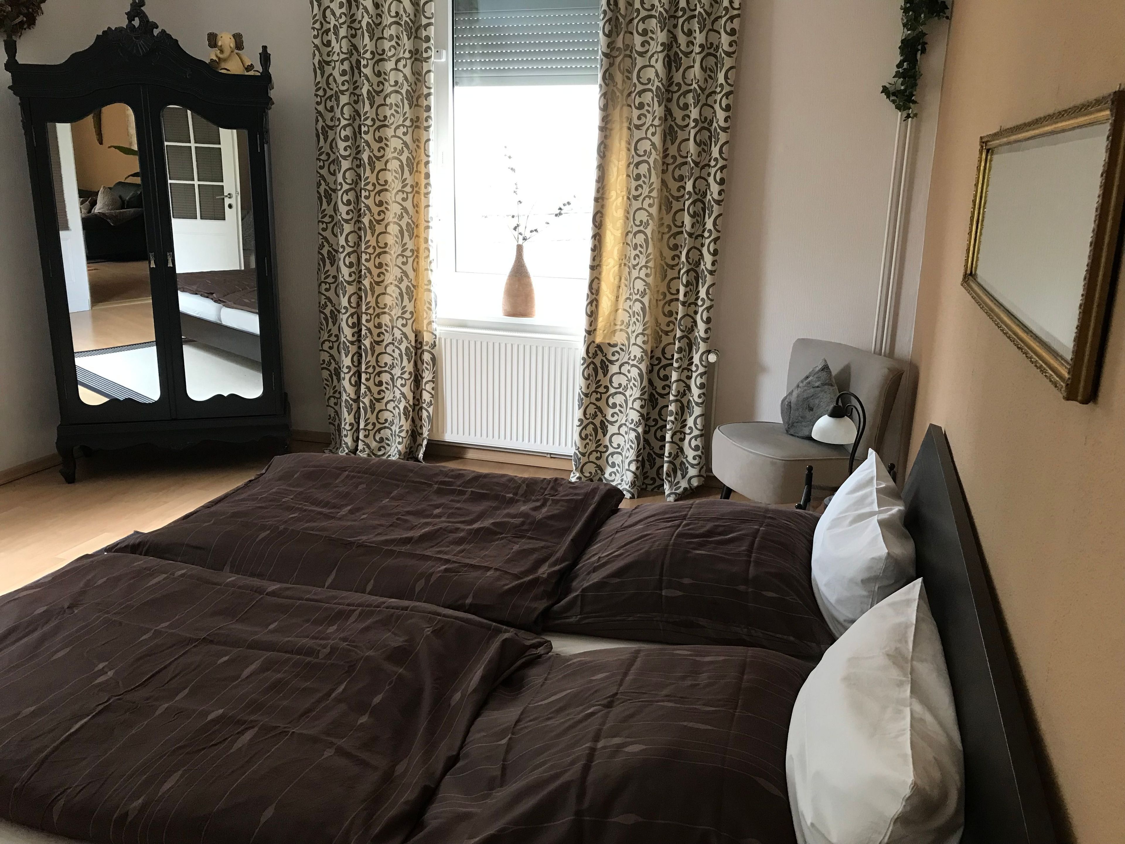 A bedroom with a large bed, a dresser, a chair, and a window with curtains.