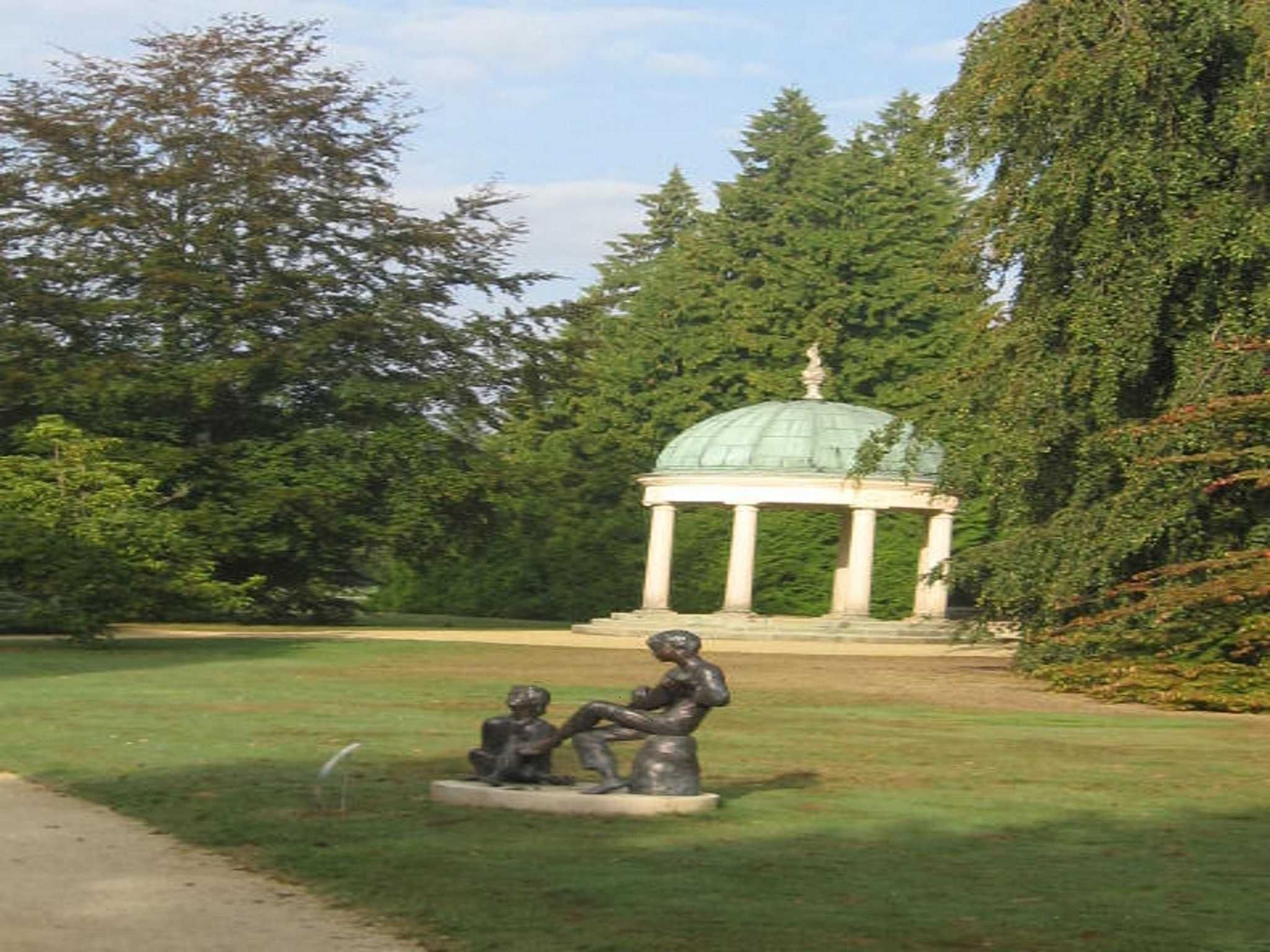 A park with a gazebo, a statue of two figures, and a pathway.