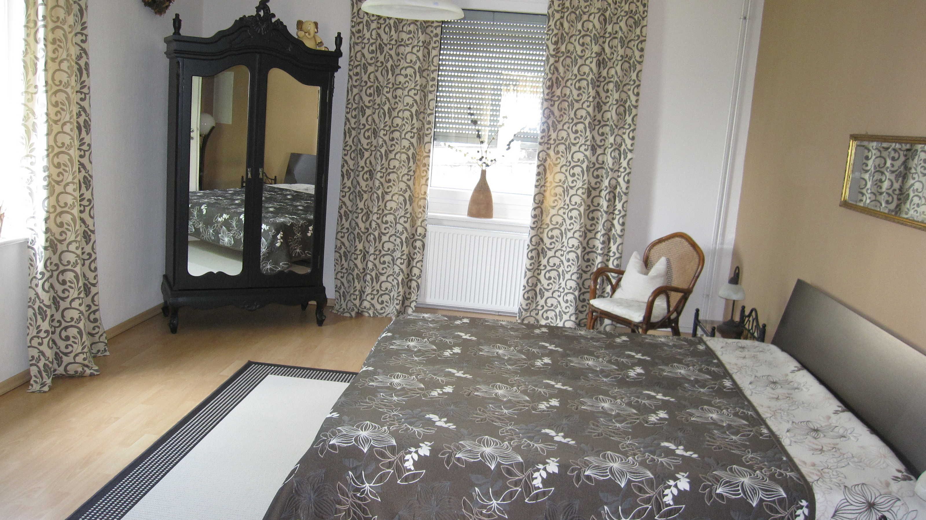 Une chambre à coucher avec un lit, une commode, une chaise et une fenêtre avec des rideaux.