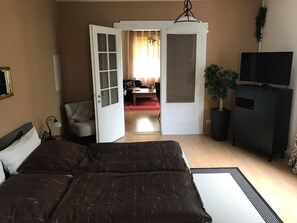 Ein Schlafzimmer mit einem Bett, einem Fernseher, einer Pflanze und einer offenen Tür zu einem Wohnbereich.
