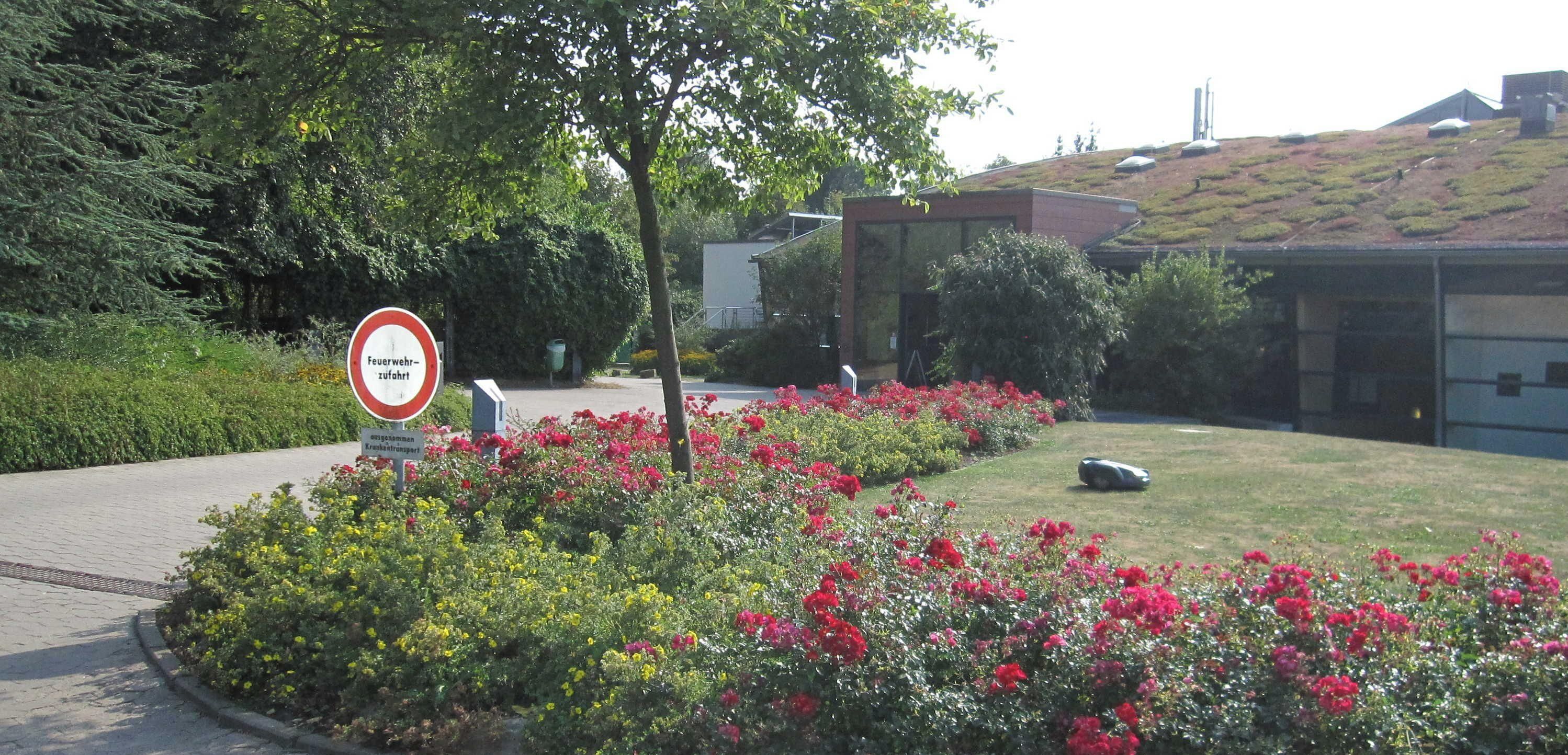 Un espace aménagé, agrémenté d’un panneau indiquant l’emplacement d’une caserne de pompiers, et entouré d’arbustes et d’arbres en fleurs.