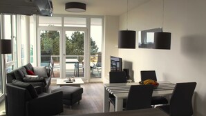 A modern living room with a sofa, coffee table, and dining area with chairs and a table. - Apartment Seaside - Whg. D-05, 3 Zi., 2 Bäder, Südbalkon (Neustadt in Holstein)