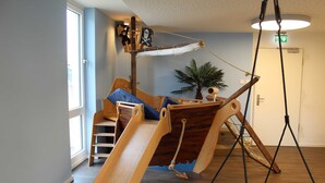A room with a wooden play area, including a slide and a hanging swing, and a door with an emergency exit sign. - Apartment Seaside - Whg. D-05, 3 Zi., 2 Bäder, Südbalkon (Neustadt in Holstein)