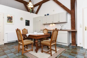 Un comedor con mesa y sillas de madera, una cocina con armarios blancos y piso de baldosas.