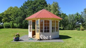 En lille, etetages pavillon med rødt tag og hvide vægge, omgivet af en græsplæne og træer.