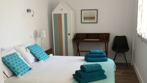 A neatly made bed with blue and white pillows, a teal throw blanket, and a wooden desk with a chair.