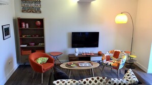 A modern living room with a sofa, a red armchair, a coffee table, a bookshelf, a flat-screen TV, and a floor lamp.