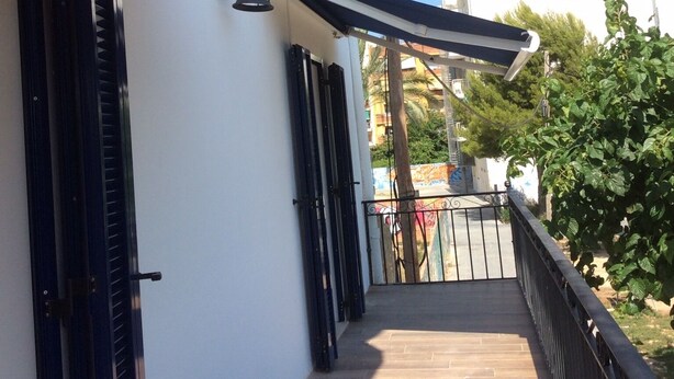 A covered outdoor area with a wooden floor, black metal railings, and a wall-mounted lantern.