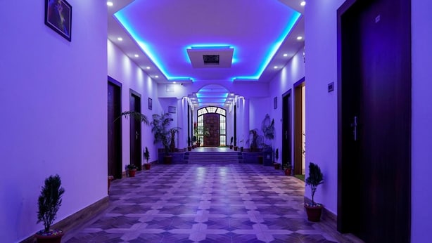 A hallway with a geometric patterned floor, potted plants, and a central staircase leading to a door with a glass panel. - Hotel Heritage (Cooch Behar)