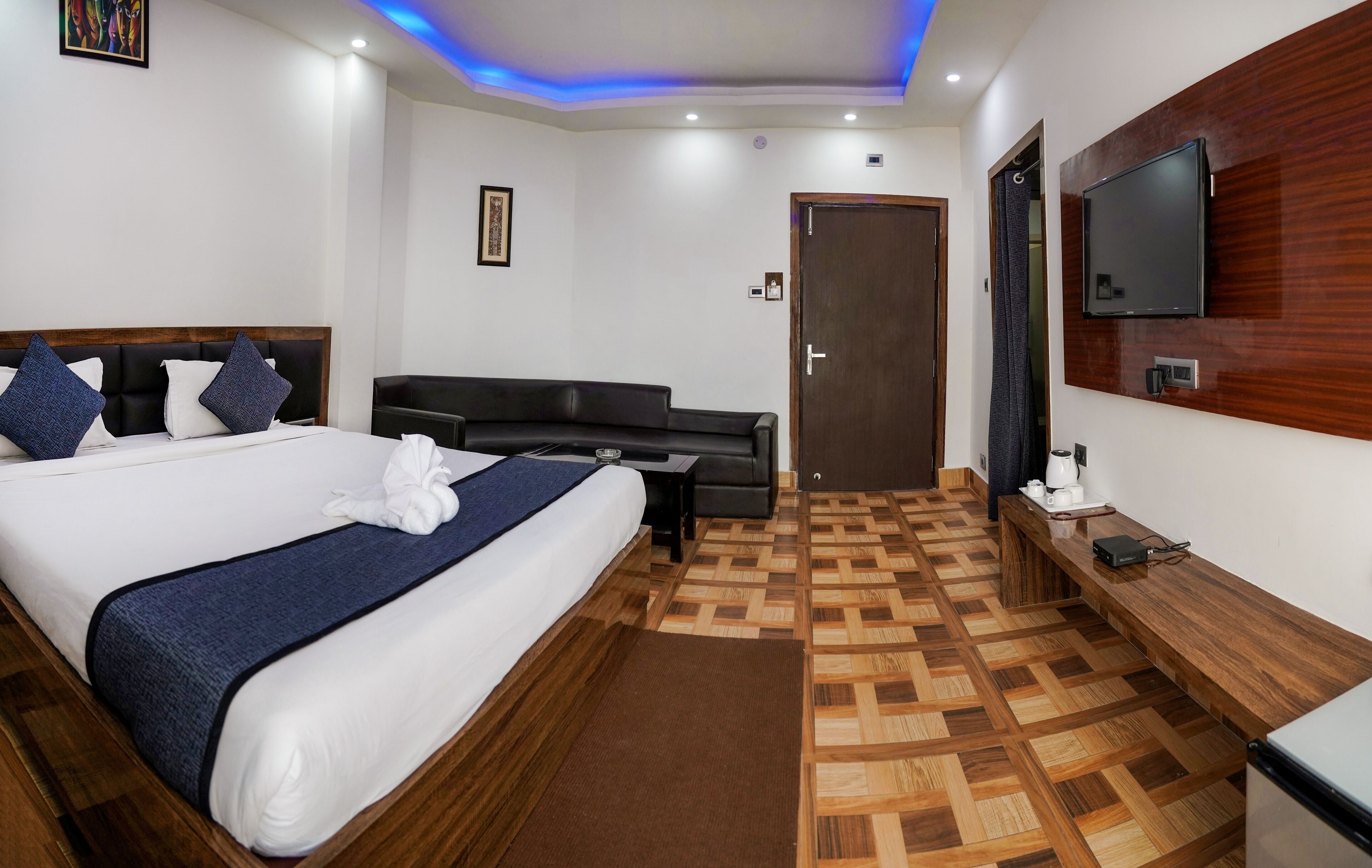 A hotel room with a large bed, a sofa, a TV mounted on the wall, and a wooden floor.