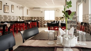 A restaurant with tables set with coasters, a vase with a rose, and a fan on the wall. - Hotel Heritage (Cooch Behar)