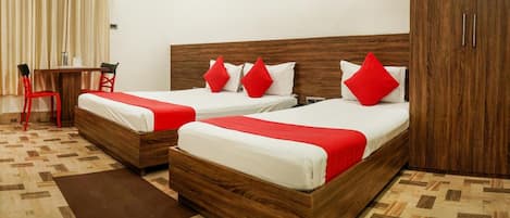 A hotel room with two wooden beds, each with red bedding and pillows, a small wooden table with chairs, and a brown rug on the floor.