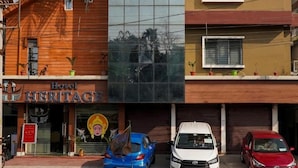 A hotel named "Heritage" with a modern facade, parked cars, and a palm tree. - Hotel Heritage (Cooch Behar)
