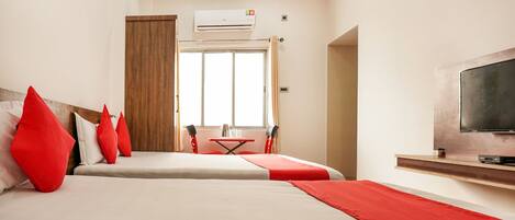 A hotel room with a bed, red pillows, a TV, and a window.