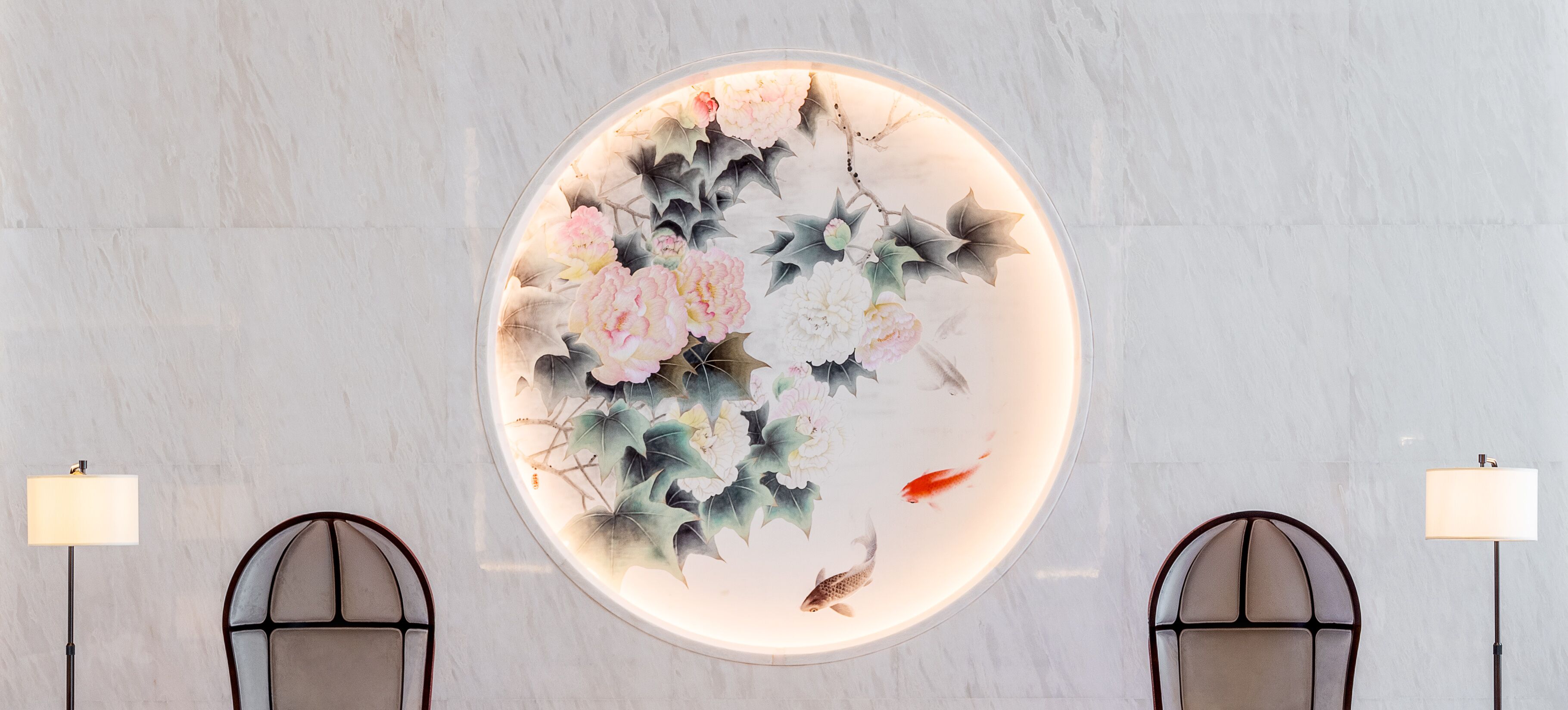 Un mural circular con motivos florales y peces koi, flanqueado por dos sillas y lámparas de pie.