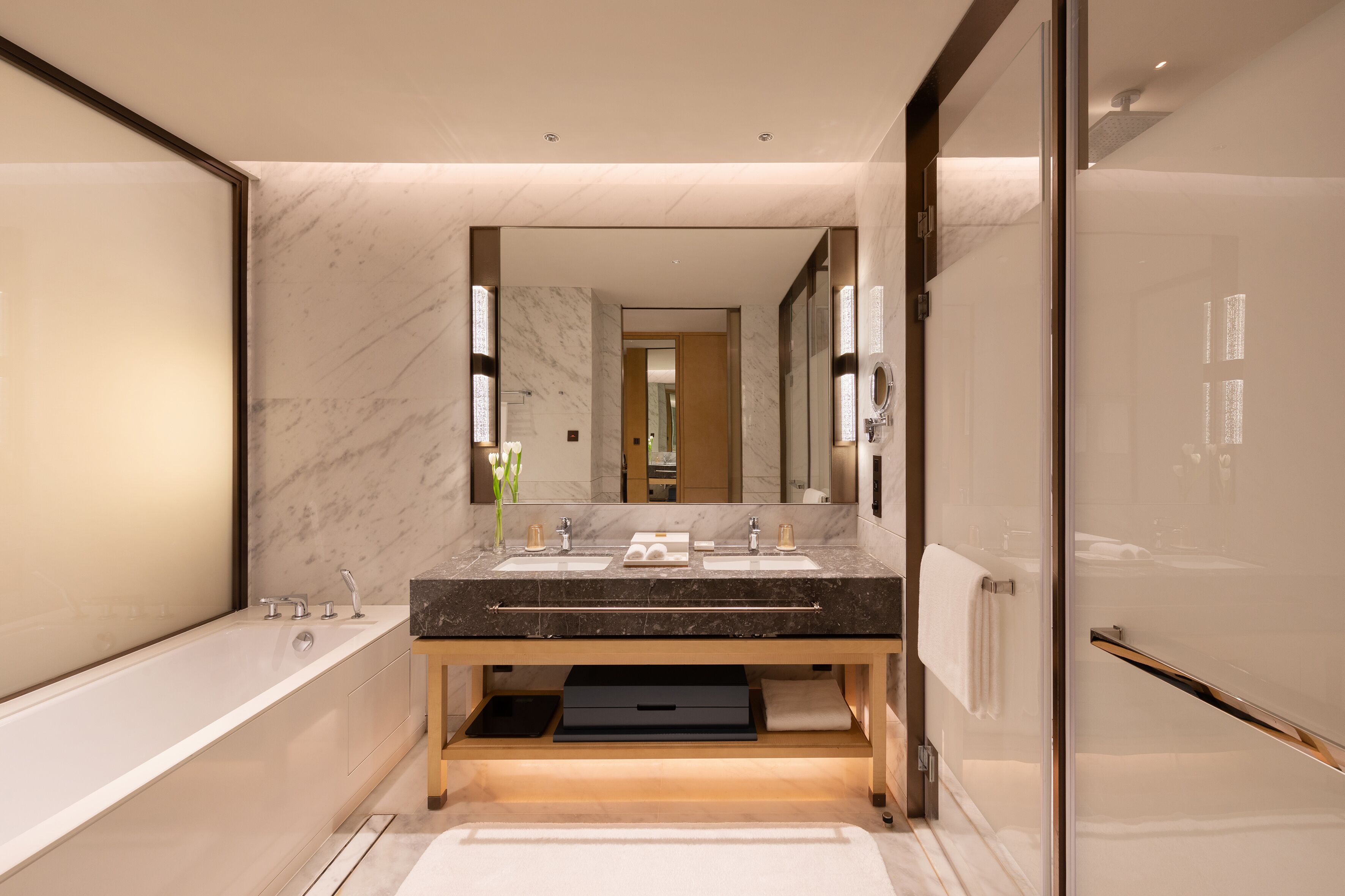 A modern bathroom with a marble vanity, dual sinks, a large mirror, and a walk-in shower.