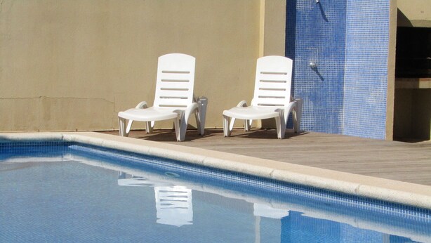 En swimmingpool med två vita solstolar och en vägg klädd med kakel.