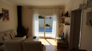 Ett vardagsrum med en soffa, en tv, en öppen spis och utsikt över en pool genom en glasdörr.
