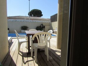 Une terrasse extérieure avec une piscine, une plateforme en bois et des chaises et une table en plastique blanc.