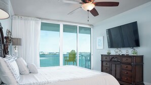 A bedroom with a large bed, a ceiling fan, a dresser, and a TV on the wall. - Exquisite Modern Bayside Three Bedroom Condo! Complimentary Boat Slip! (Orange Beach)