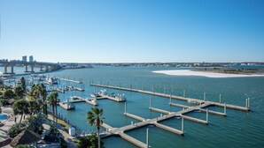 A marina with docks and boats, a bridge in the background, and a sandy beach area. - Exquisite Modern Bayside Three Bedroom Condo! Complimentary Boat Slip! (Orange Beach)
