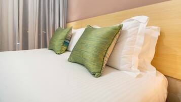 A neatly made bed with white linens and green striped pillows, a wooden headboard, and a window with sheer curtains.
