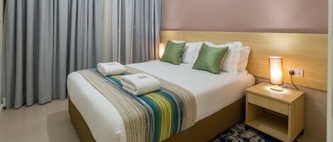 A hotel room with a bed, nightstands, a lamp, and a window with curtains.