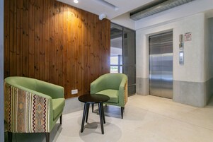 A lobby with two green armchairs, a small round table, and an elevator.