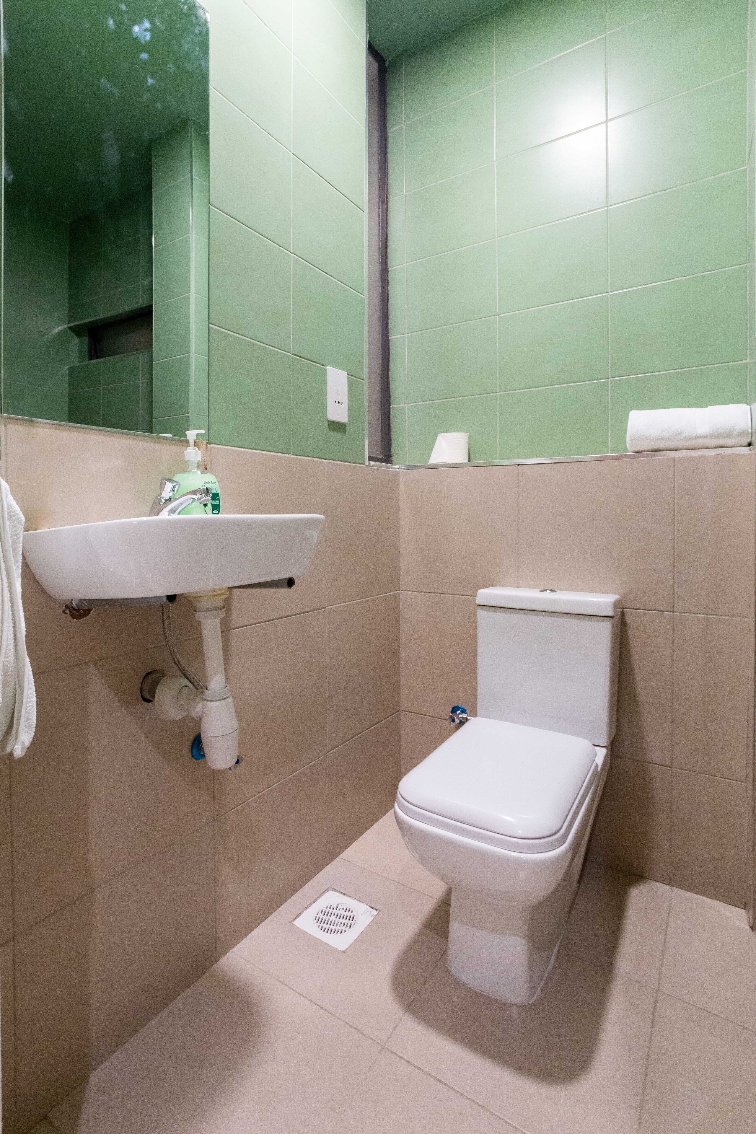 Een kleine badkamer met toilet, wastafel en groene betegelde wanden.