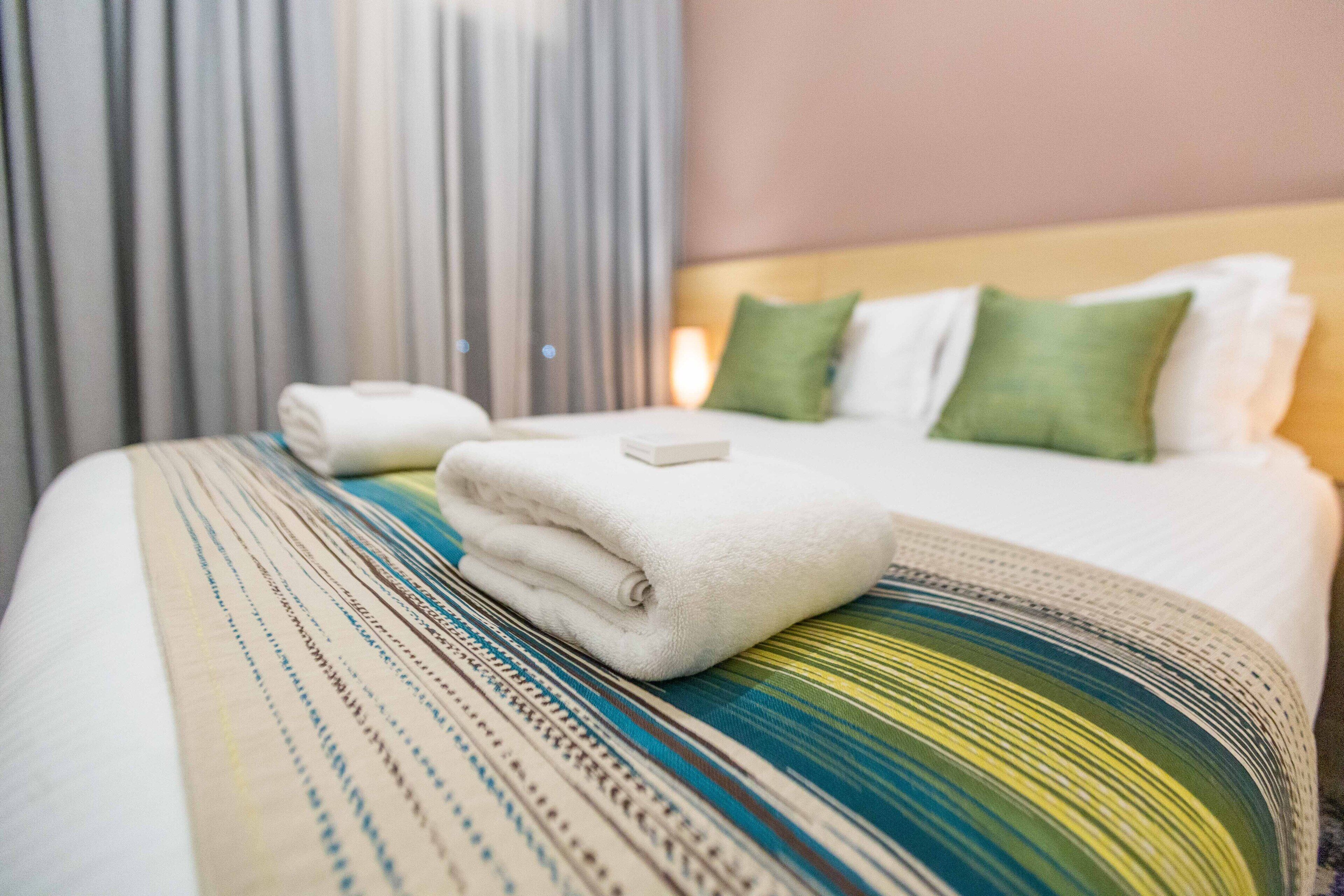 A neatly made bed with a striped bedspread, pillows, and a folded towel.