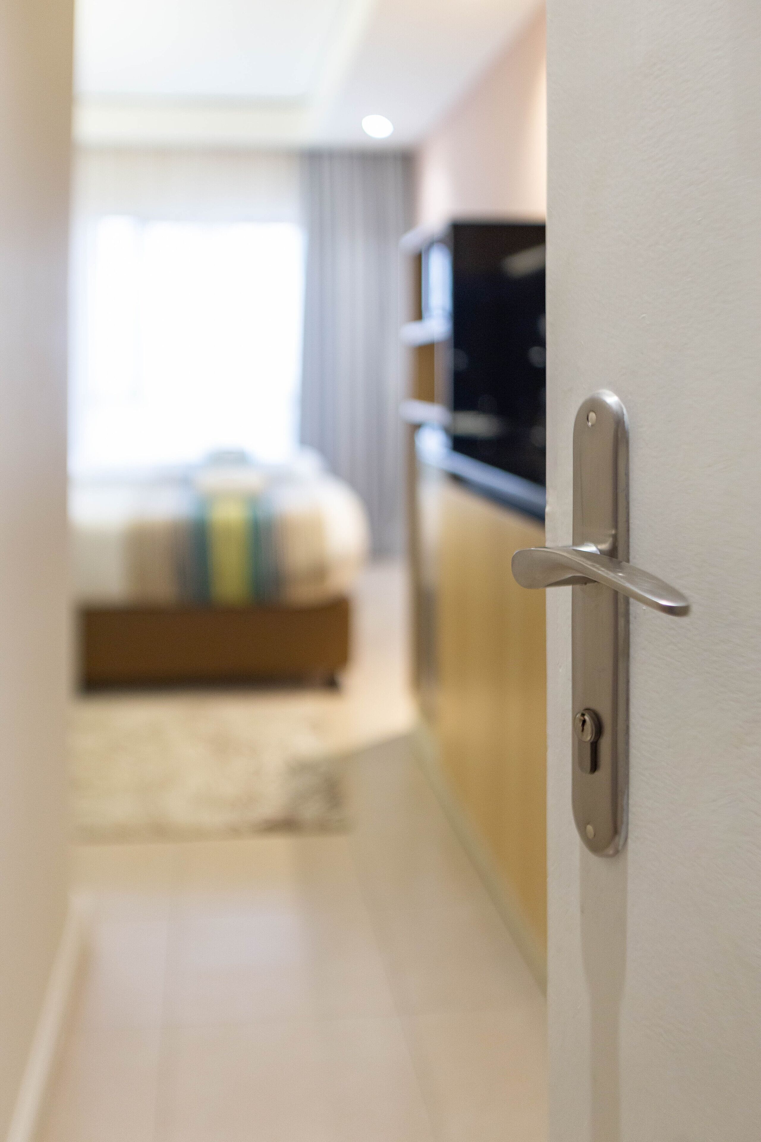 A hotel room with a bed, a TV, and a door with a handle.