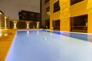 A swimming pool with a clear blue surface, surrounded by a building with multiple windows and balconies.