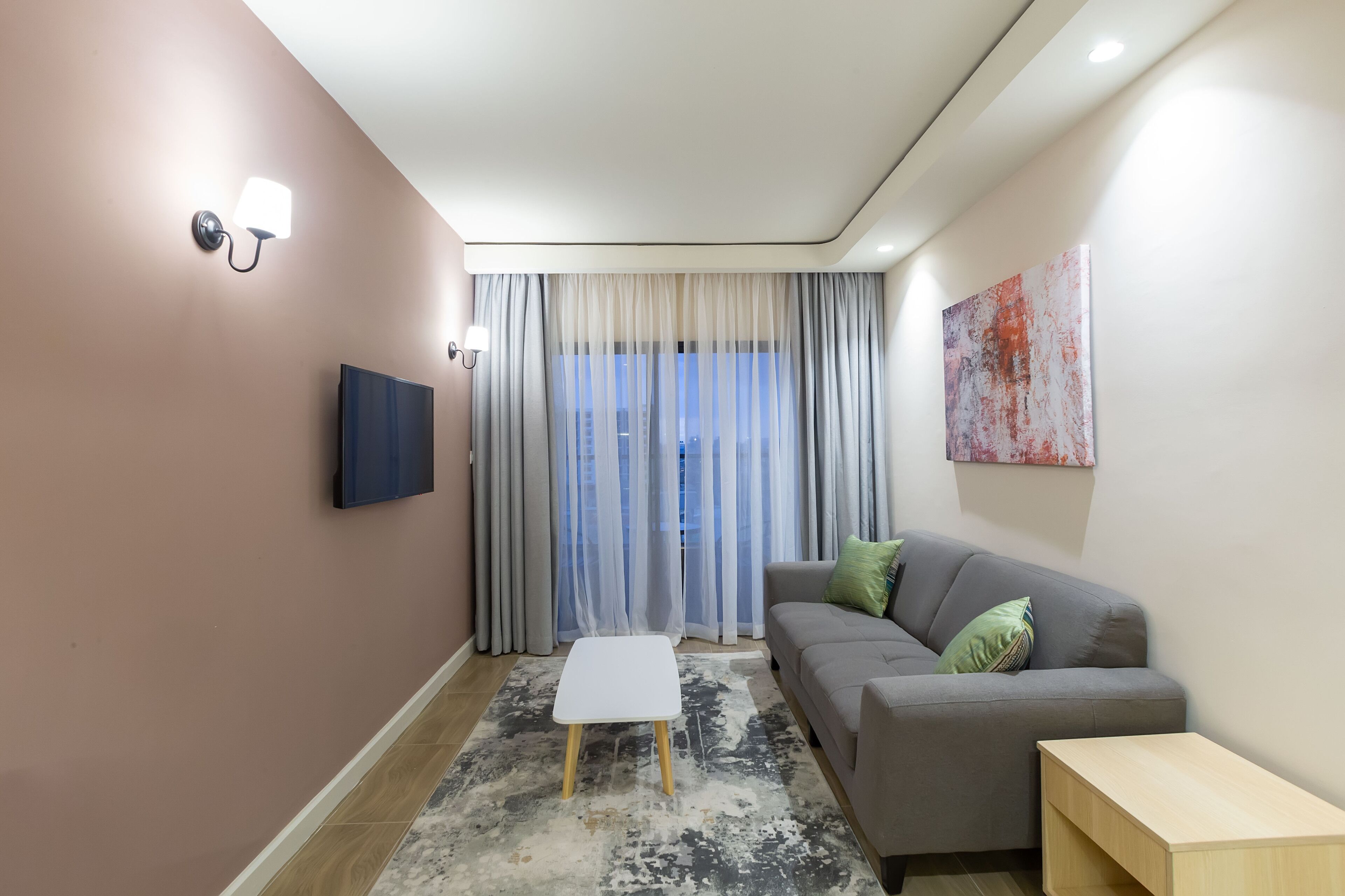 A modern living room with a grey sofa, a small white table, and a TV mounted on the wall.