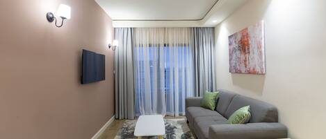 A modern living room with a grey sofa, a small white table, and a TV mounted on the wall.