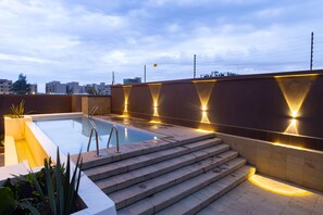 A rooftop swimming pool with steps leading down to the water, surrounded by a low wall with integrated lighting. - Kozi Suites Nairobi Airport (Syokimau)