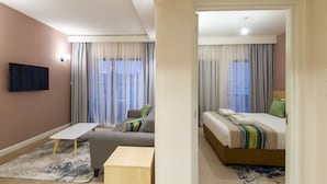 A modern hotel room with a sofa, a small wooden table, a bed with a striped blanket, and a TV mounted on the wall.