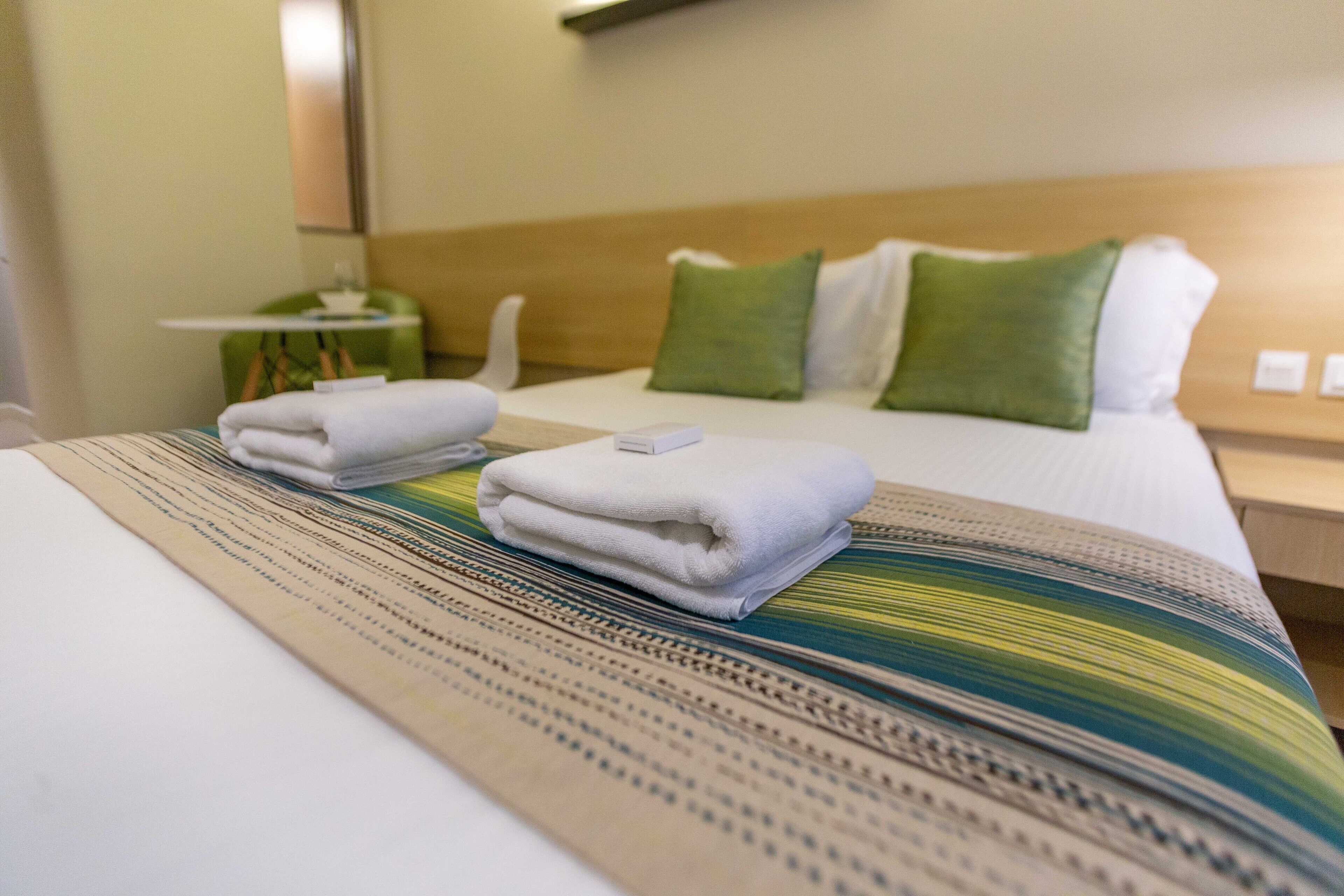 A neatly made bed with folded towels and a patterned bedspread.