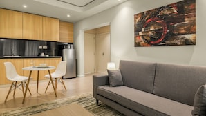 A modern living room with a grey sofa, white chairs, a round table, and a kitchen in the background.
