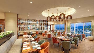 Un restaurante espacioso con varias zonas de comedor, un gran mural y vista al mar.