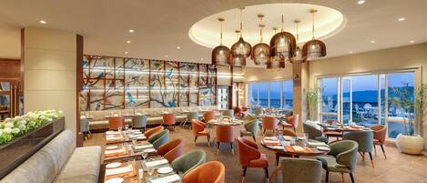 A spacious restaurant with multiple dining areas, a large mural, and a view of the sea.