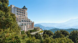 A multi-story hotel with a tower-like structure, surrounded by lush greenery and mountains in the background. - Welcomhotel by ITC Hotels, Tavleen, Chail (Shimla)