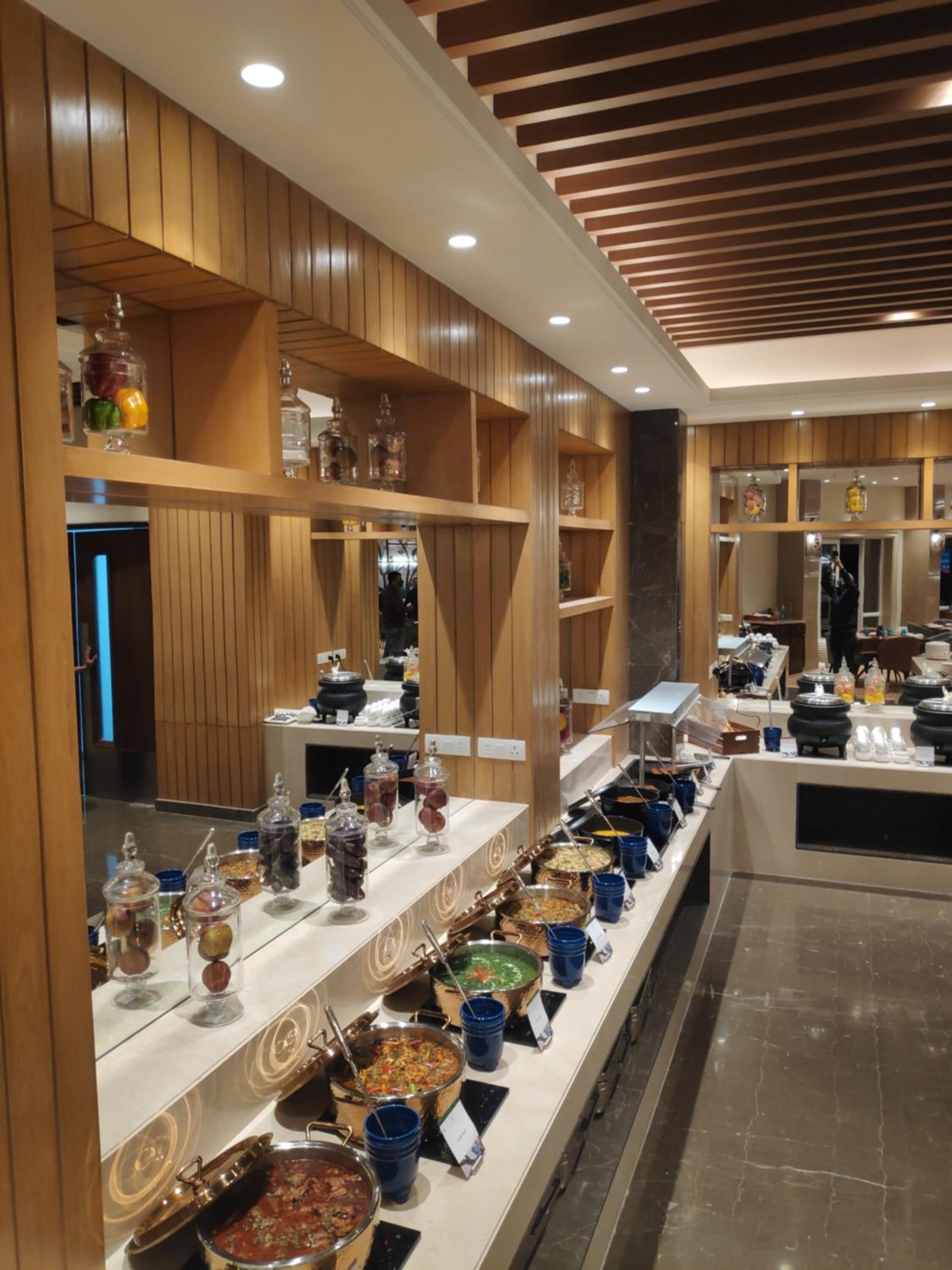 A buffet setup with various food stations, wooden paneling, and a modern ceiling design.