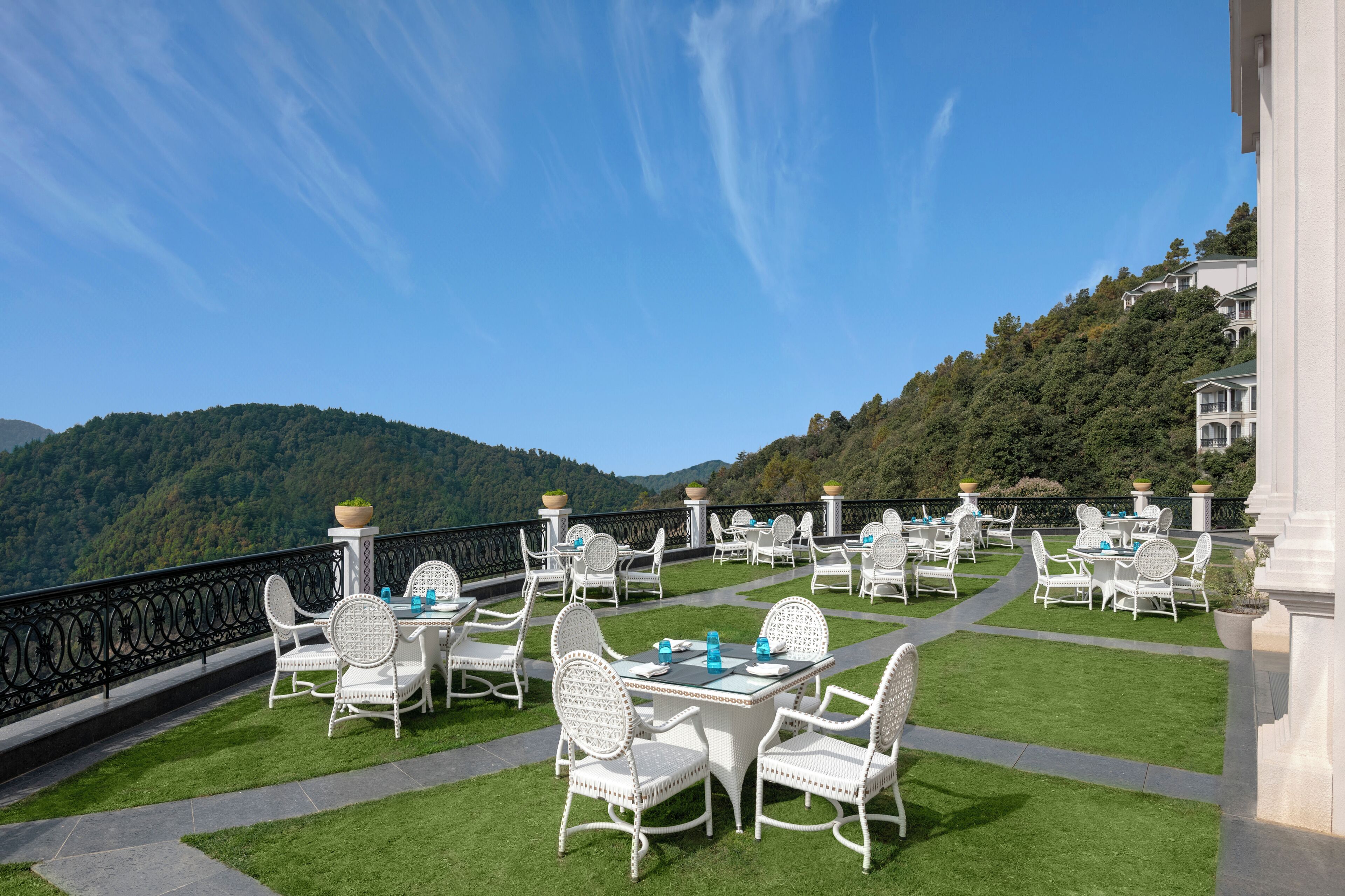 Un espacio exterior para comer con mobiliario de ratán blanco y una vista panorámica de la montaña.