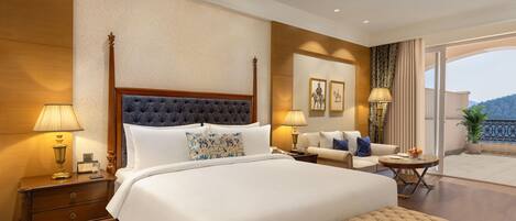 A hotel room with a large bed, bedside tables, a sofa, a small table, and a balcony with a view.