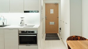 A modern kitchen with a dishwasher, oven, and coffee maker. There is a wooden door with a sign on it, and a black chair with a tiger print cushion. - Time Apartments Ylistönmäki (Jyväskylä)